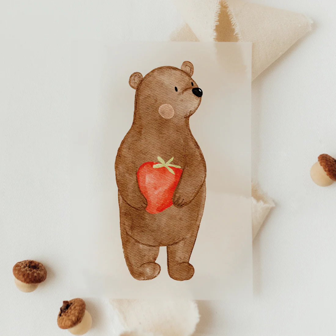 Hier sieht man auf diesem Bügelmotiv eine Bären mit Erdbeere in den Händen. Er schaut zur Seite und hat Pauschbäckchen. Es handelt sich um ein Kindermotiv.
