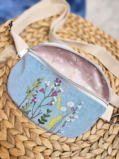 Hier sieht man in Detailansicht die filigrane Stickerei der Tasche mit Wildblumen. Die Blumen sind in hellem Creme, pink und zartem Blau. Abgerundet wird das Motiv durch dezente Grüntöne und ergänzt durch eine gelbe Ähre.