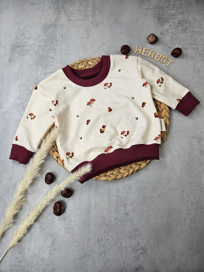 Kinderpullover mit beigem Pilzmotivstoff und dunkelroten Bündchen
